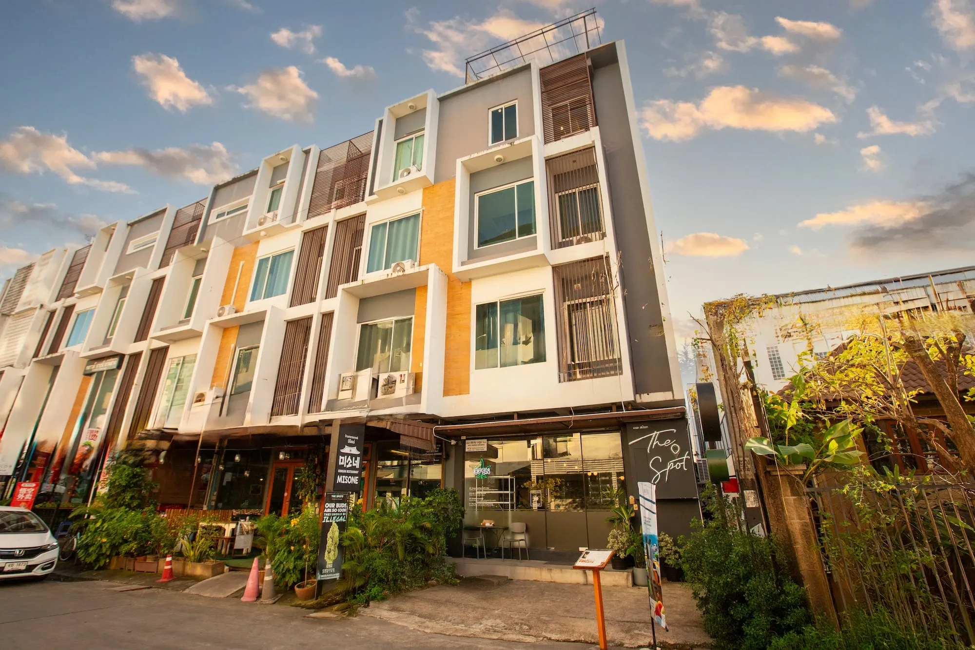 The building at 36 Nimmana Haeminda Road Lane 11 at golden hour. Five floors, with The Spot's sign and shopfront on the ground floor and a rooftop railing at the top.