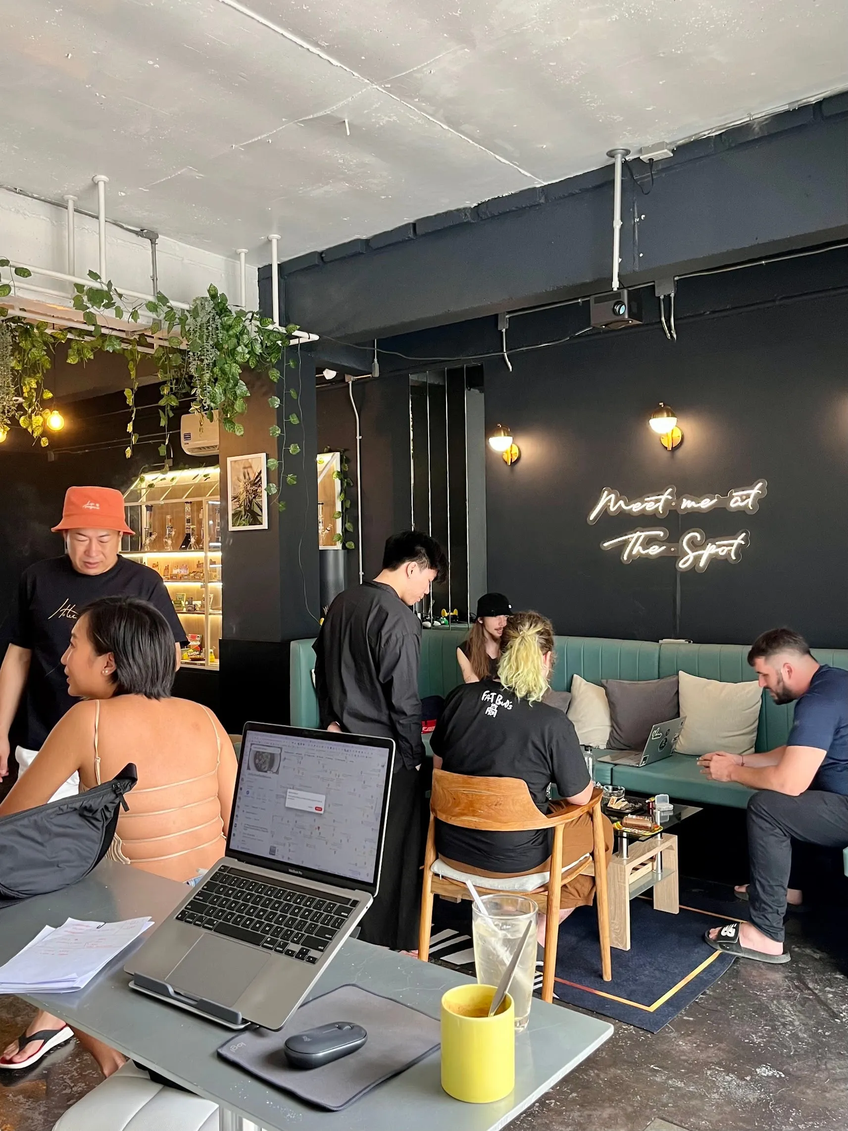 People working on laptops at a table in the lounge, plants and the neon sign behind them