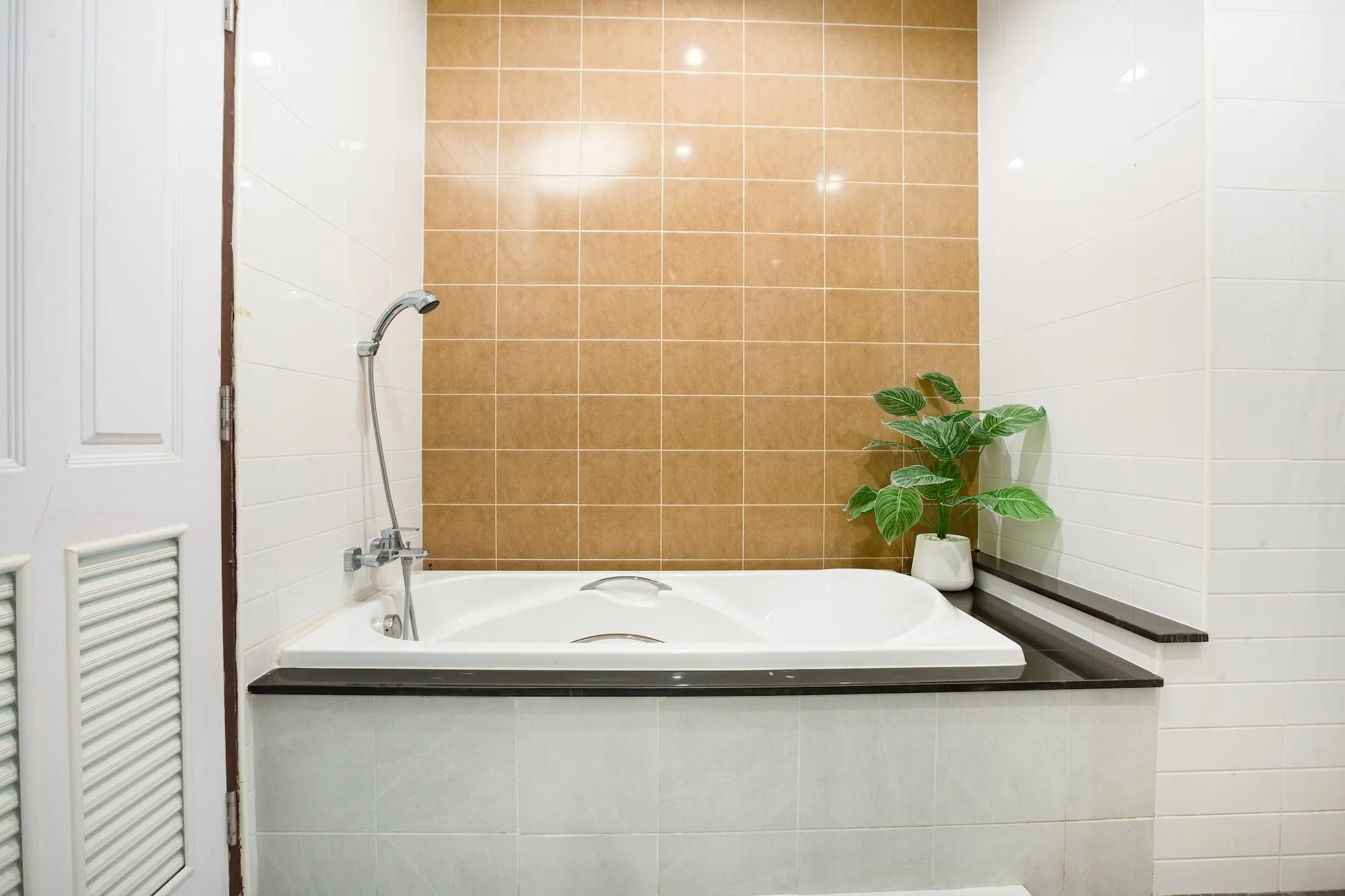 The bathroom in a Safehouse apartment, a full bathtub against tiled walls with a plant beside it