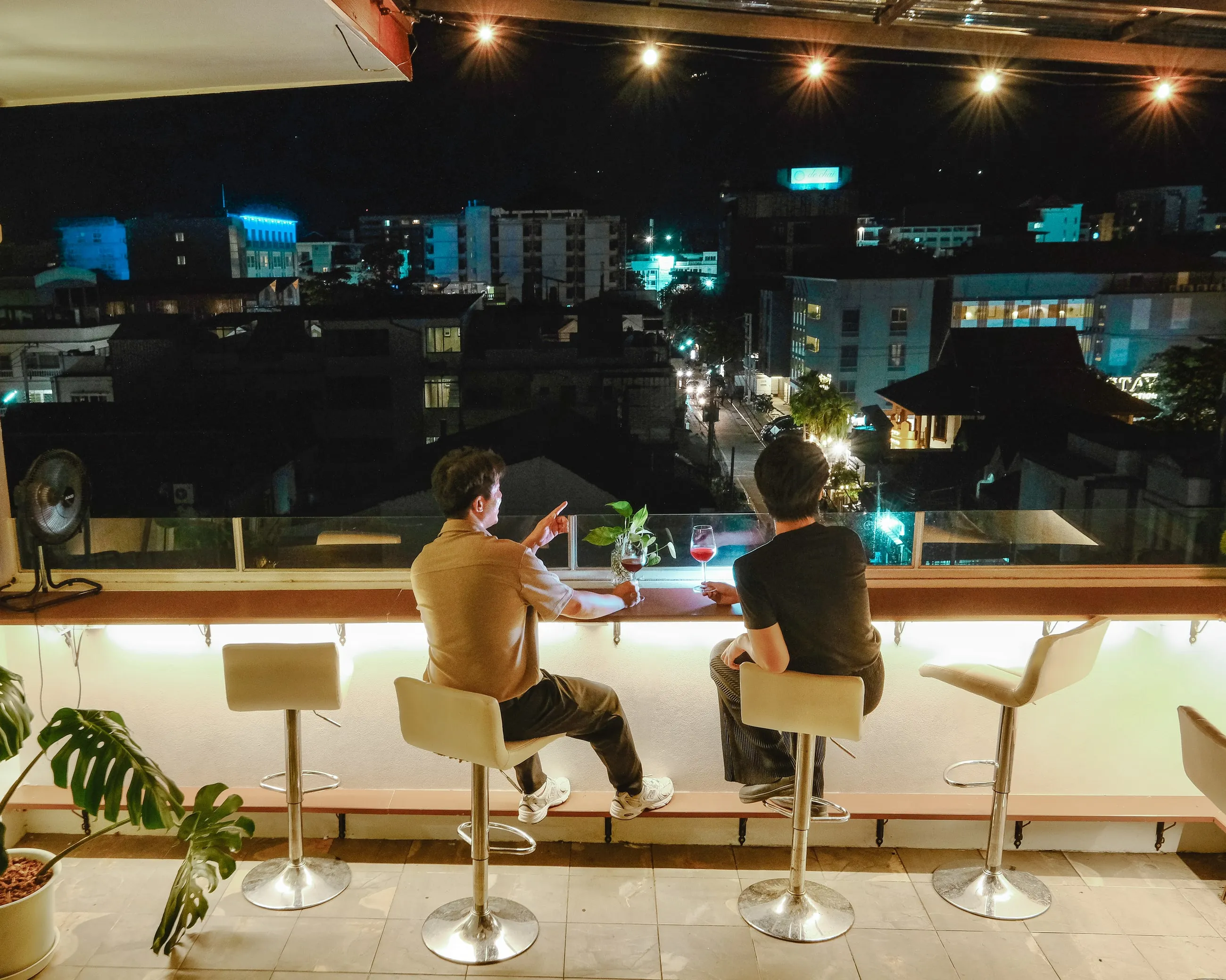 The Sway CNX rooftop counter at night, two people ordering, Chiang Mai city lights spread out behind